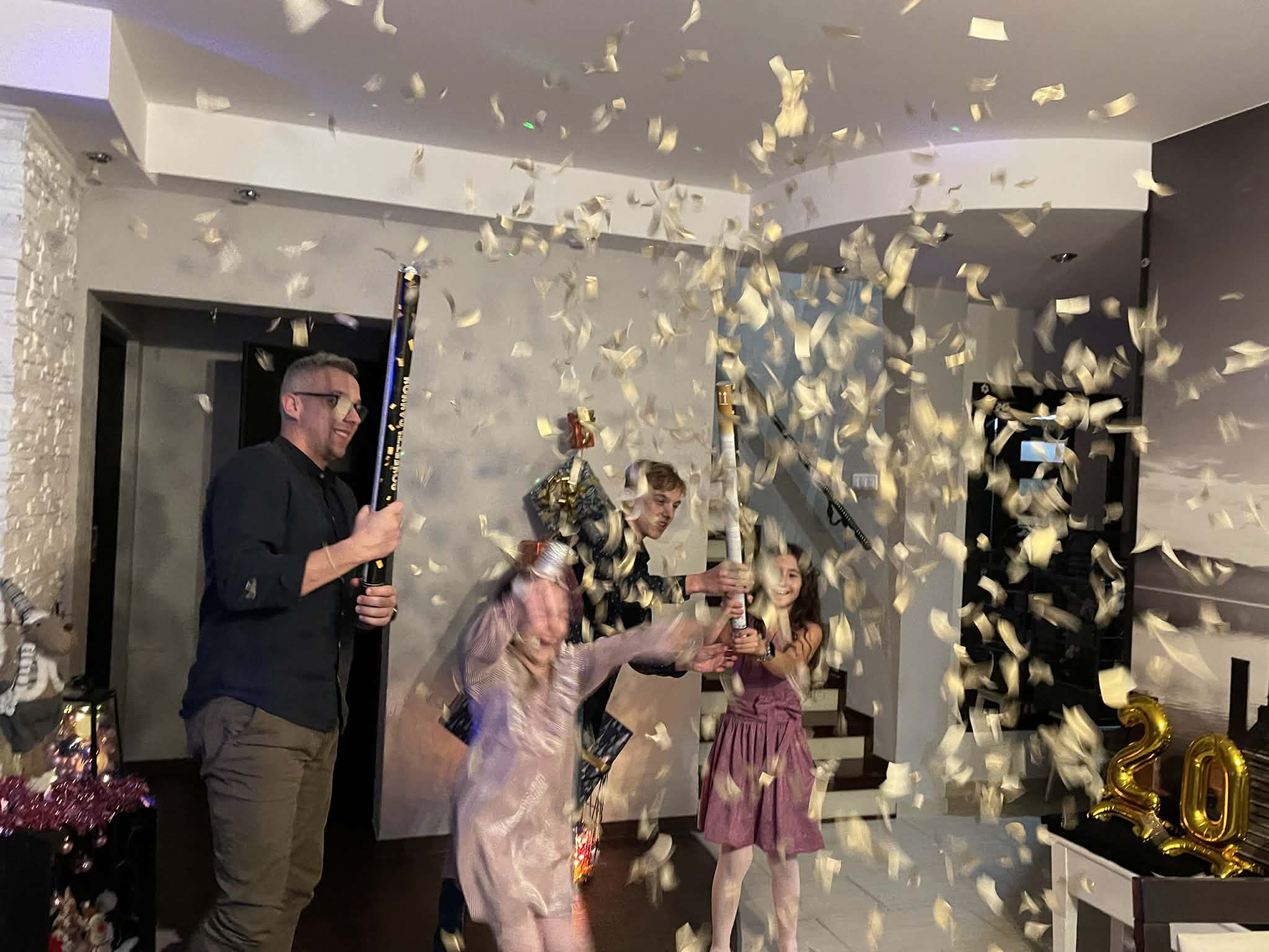 Rodzinne świętowanie sylwestra w domu, ojciec i dzieci wspólnie strzelają konfetti.