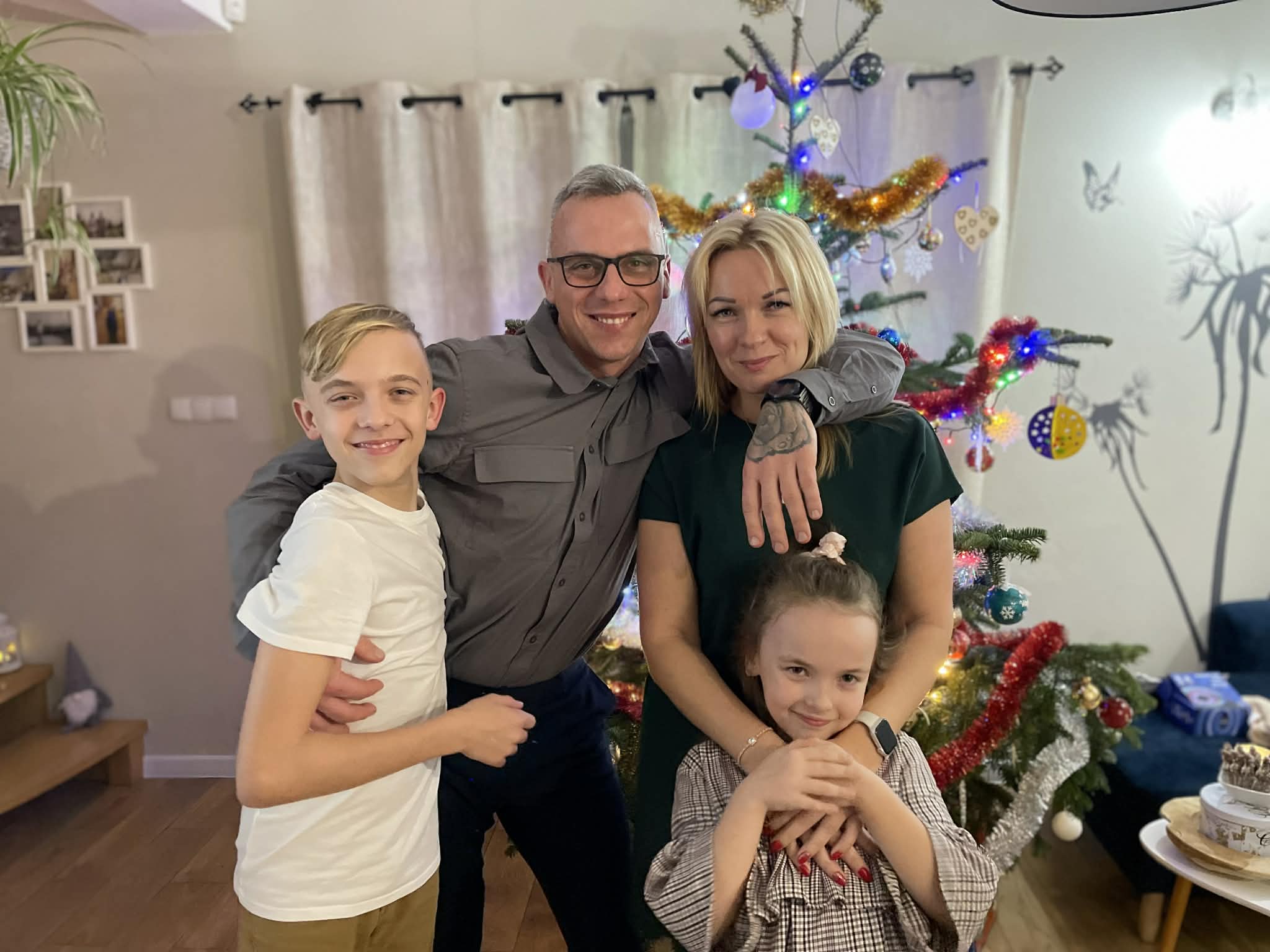 Portret uśmiechniętej rodziny podczas domowej zabawy sylwestrowej, w tle widać choinkę.