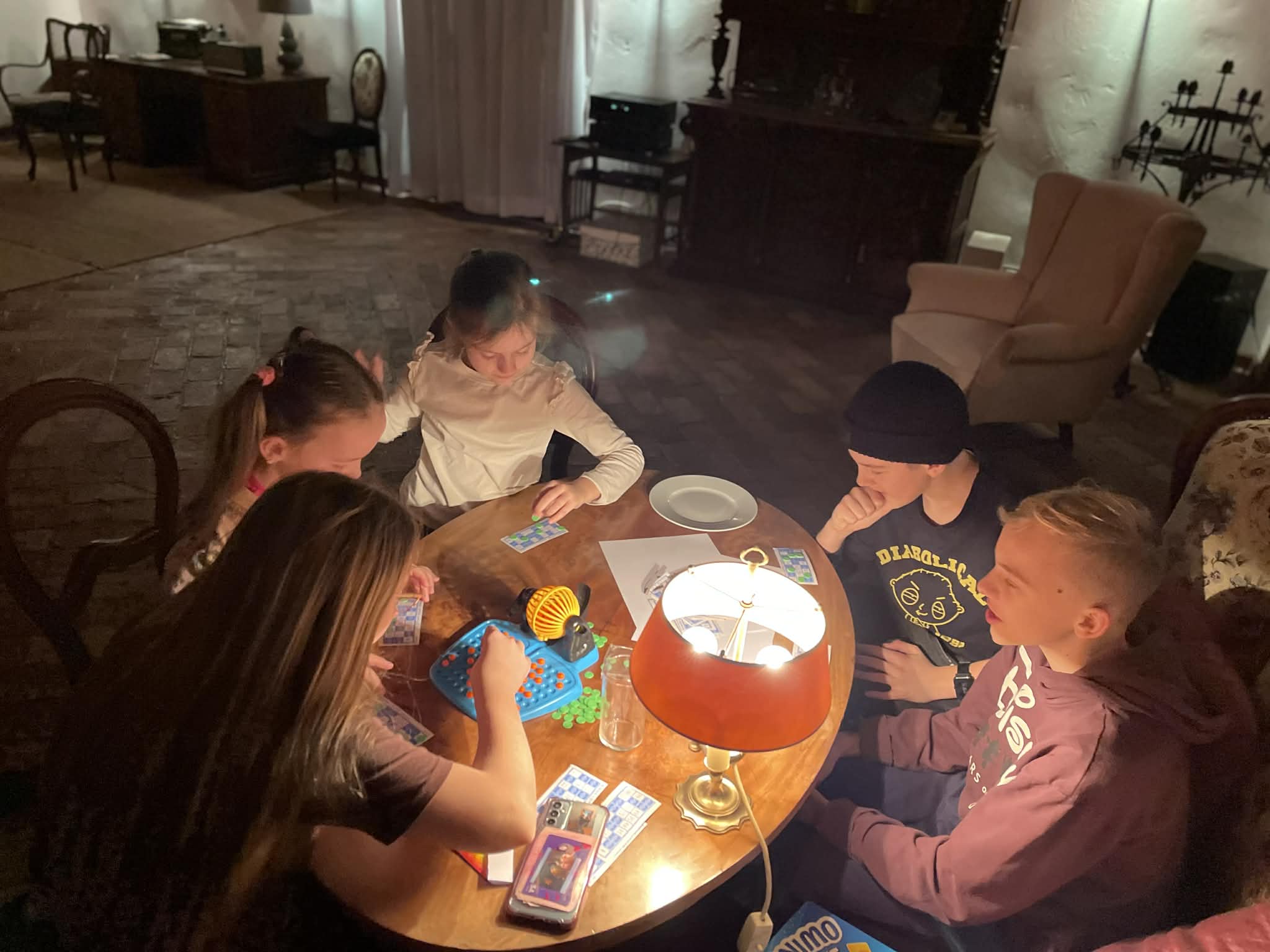 Grupa dzieci i nastolatków siedzi przy owalnym stole i gra w grę planszową podczas sylwestra.