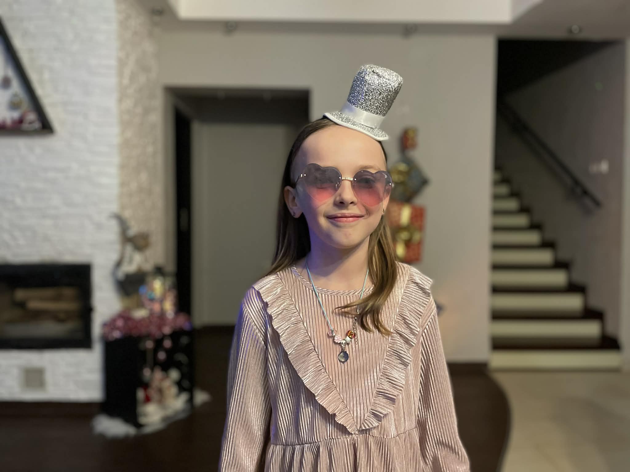 Dziewczynka w sylwestrowym kapelusiku i okularach w kształce serca pozuje do zdjęcia podczas rodzinnej imprezy sylwestrowej.