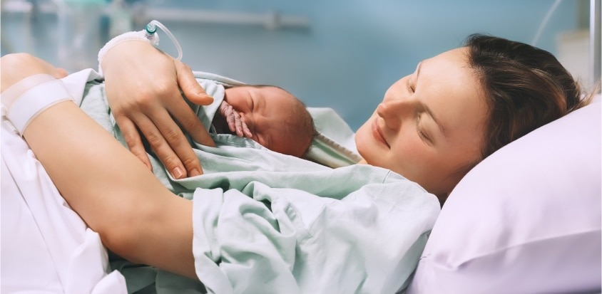 Mama leży na szpitalnym łóżku razem z noworodkiem po badaniach przesiewowych