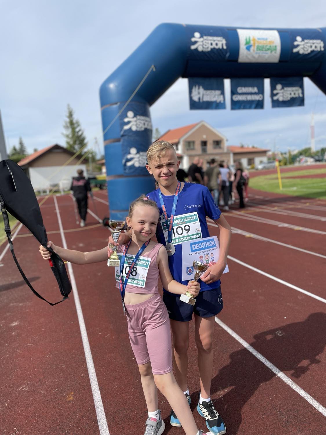Chłopiec i dziewczynka z medalami i pucharem pozują na bieżni lekkoatletycznej